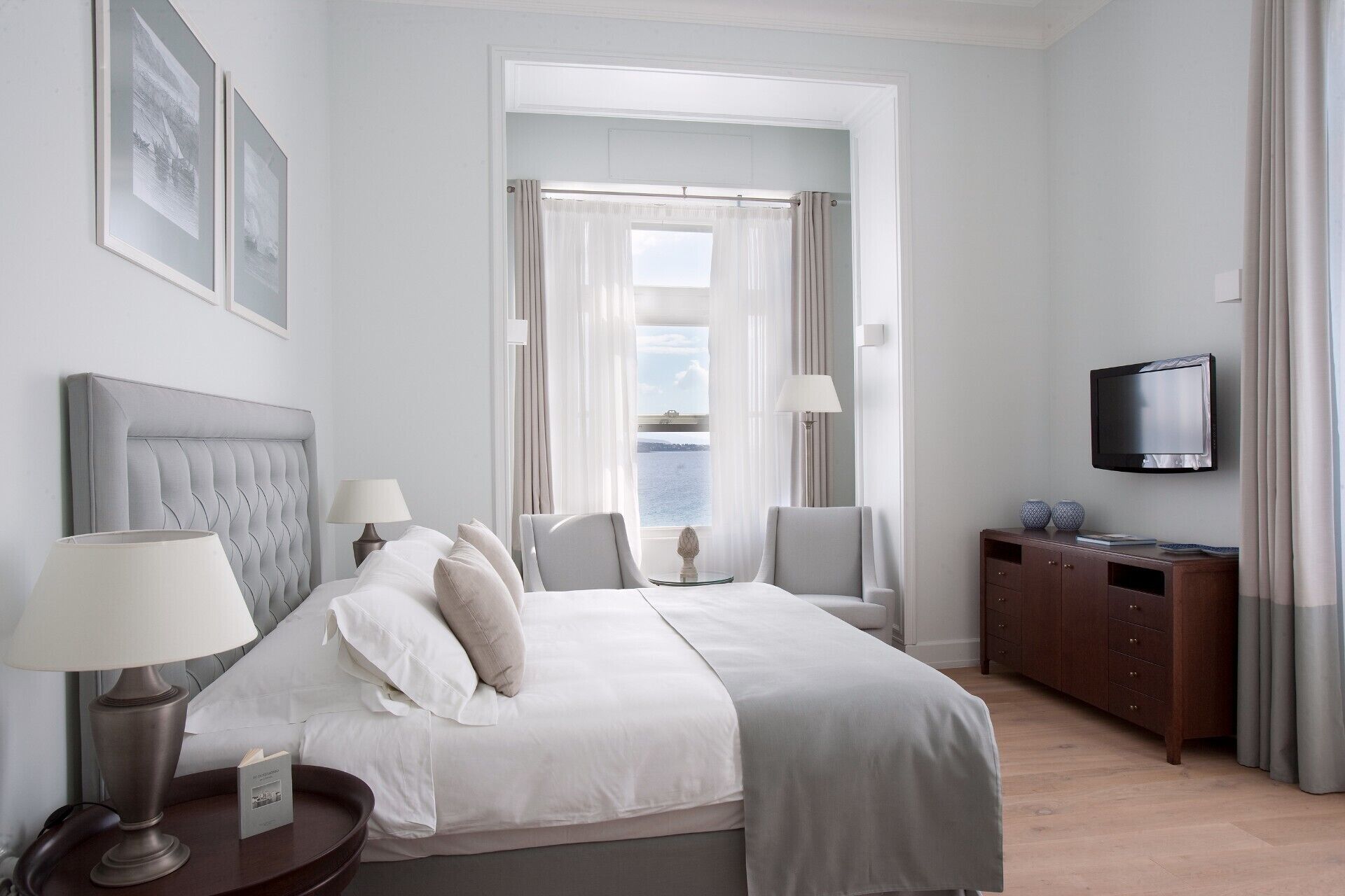Una habitación de hotel con cama, dos sillas, televisor y vista al mar.
