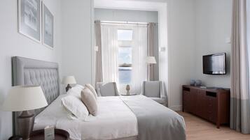 Una habitación de hotel con cama, dos sillas, televisor y vista al mar.