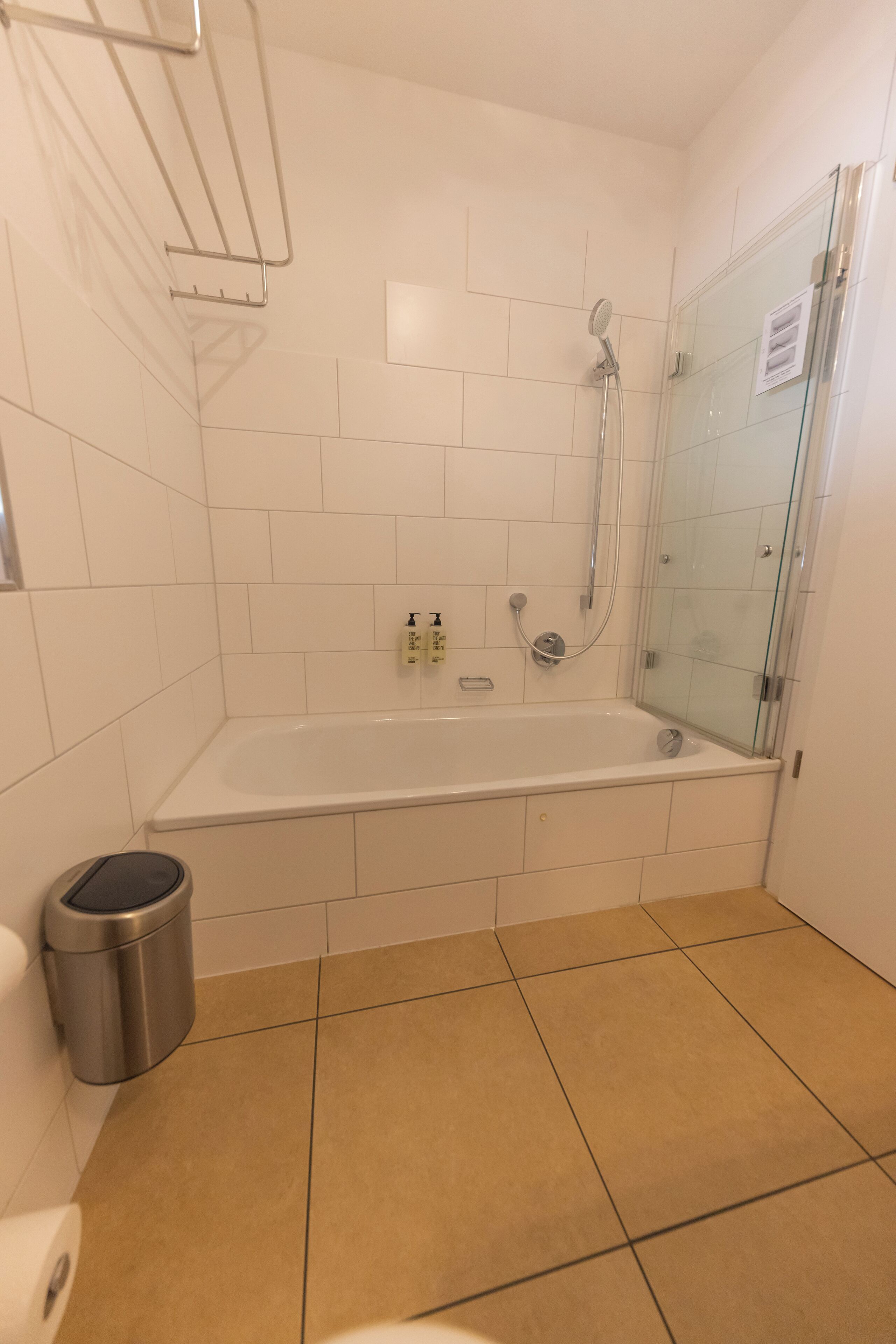 Un baño con ducha de vidrio, una bañera blanca y un cubo de basura.