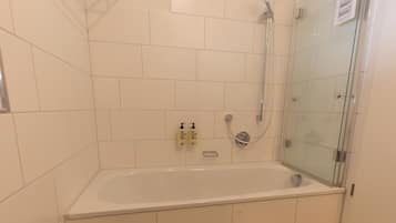 Un baño con ducha de vidrio, una bañera blanca y un cubo de basura.