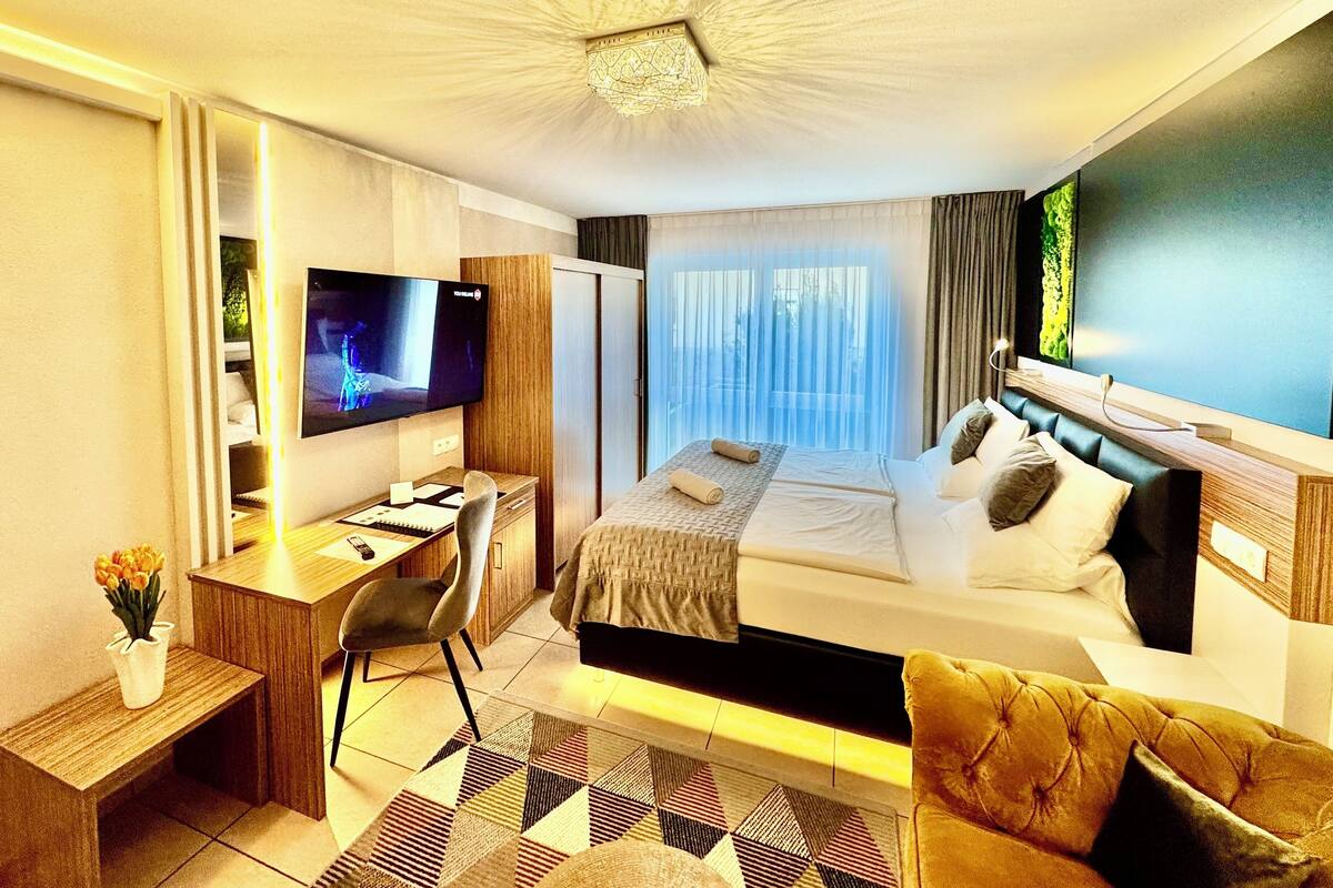 Ein Hotelzimmer mit Bett, Schreibtisch, Sessel, Fernseher und Blick ins Freie.