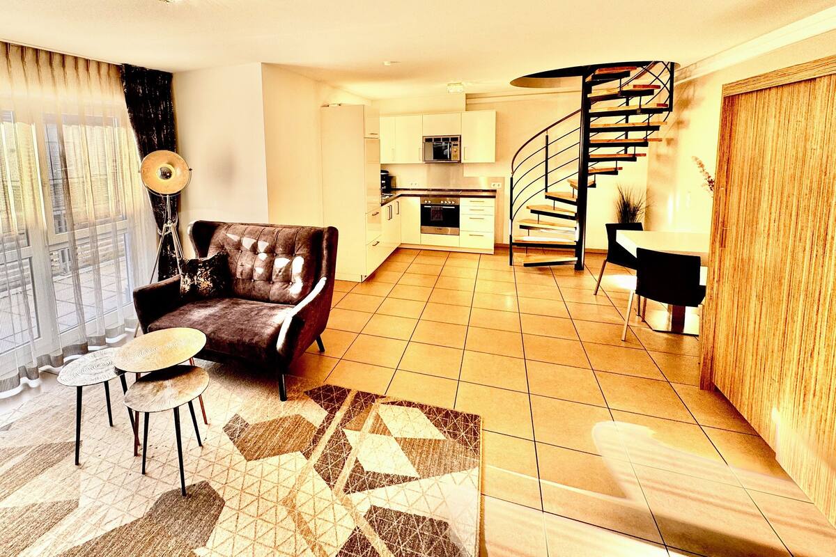 Ein modernes Wohnzimmer mit einer Couch, einem Couchtisch und einer Wendeltreppe, die in eine Küche führt.