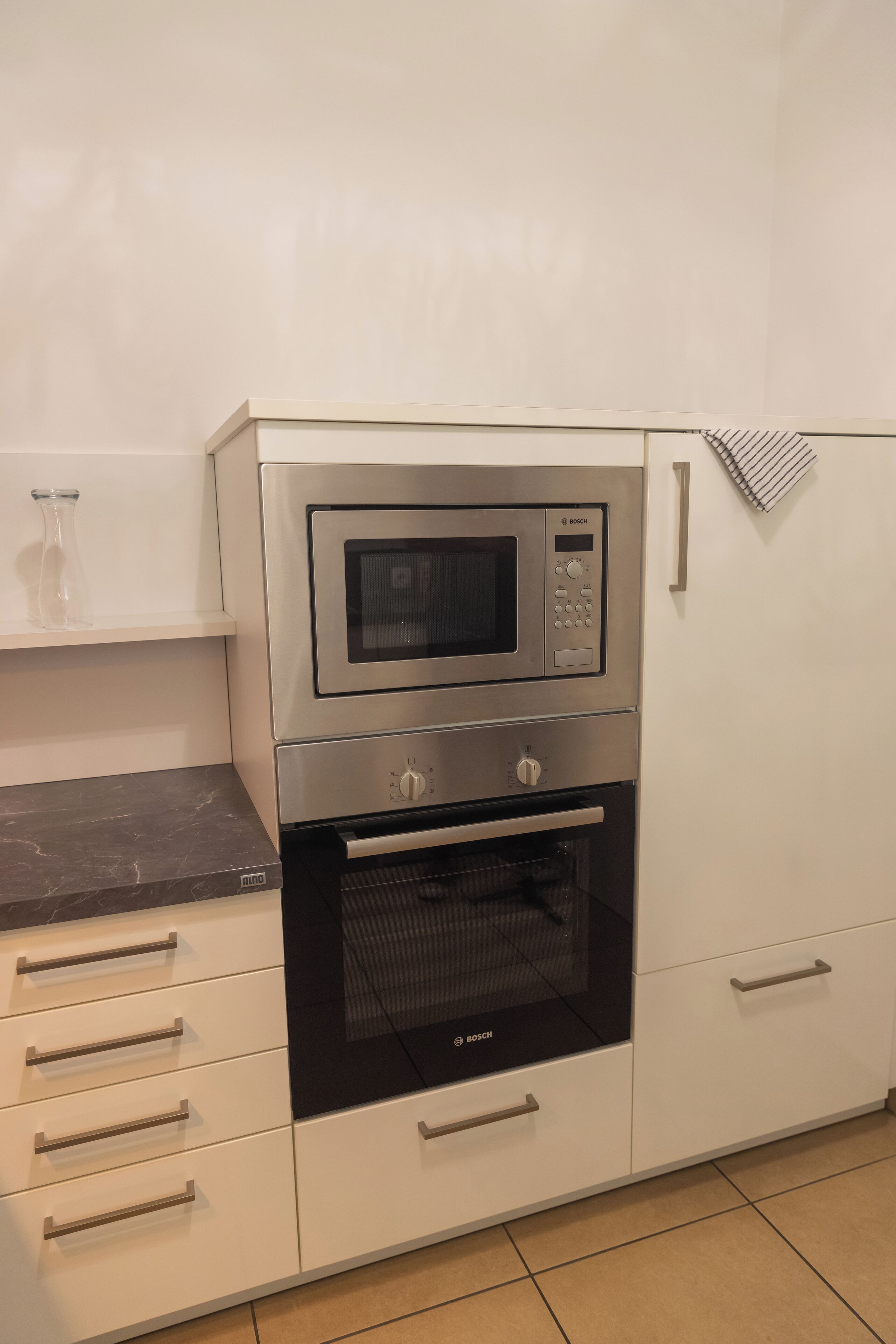 Eine Küche mit einer Bosch-Mikrowelle und einem Backofen, weißen Schränken und einer Marmorarbeitsplatte.