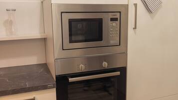 Eine Küche mit einer Bosch-Mikrowelle und einem Backofen, weißen Schränken und einer Marmorarbeitsplatte.
