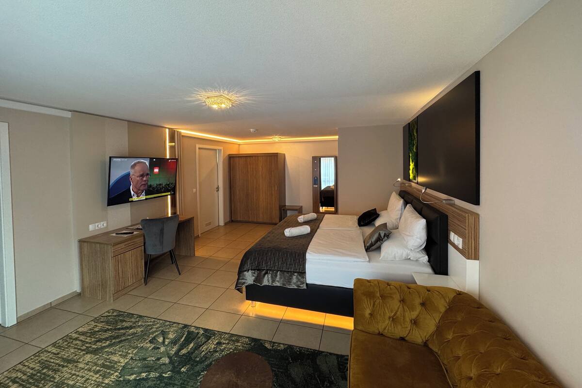 Ein modernes Hotelzimmer mit einem großen Bett, einer Couch, einem Fernseher und einem Schreibtisch.
