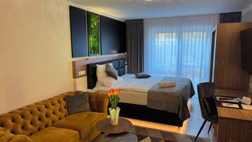 A hotel room with a sofa, a bed, a desk, and a view of the outdoors.