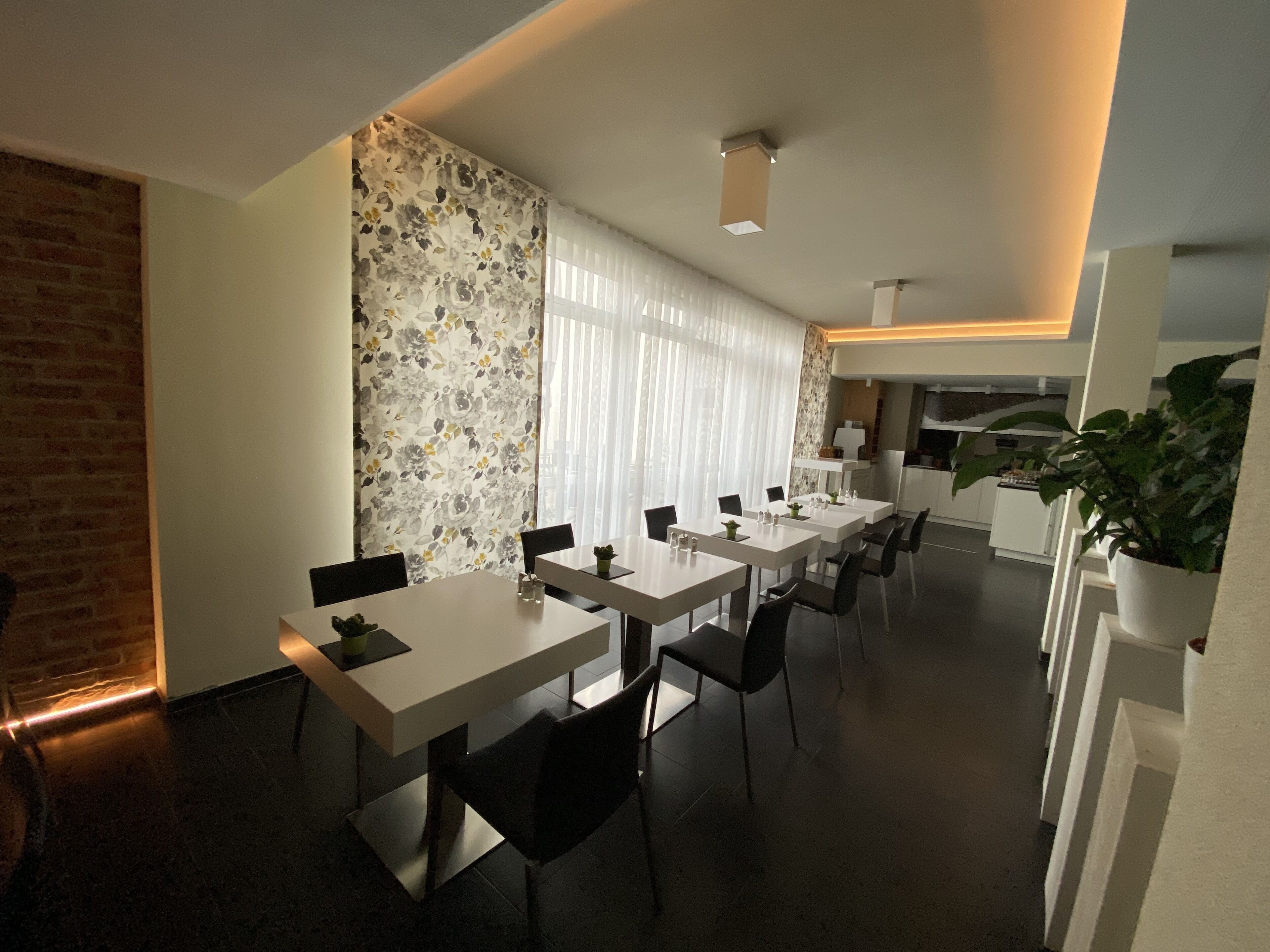 A modern dining area with white tables and chairs, a brick wall, and a floral wallpaper.