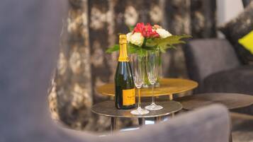 A bottle of champagne, two glasses, and a vase with flowers on a round table.