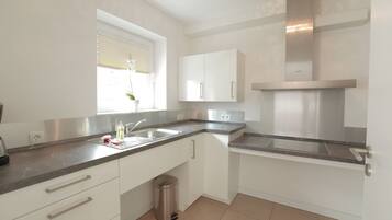 A modern kitchen with white cabinets, a stainless steel range hood, and a window with blinds.