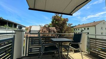 Ein Balkon mit Tisch und Stühlen, einem Metallgeländer und Blick auf Gebäude und Bäume.