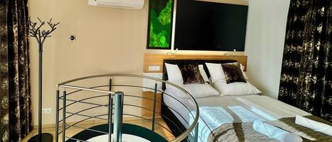 Habitación de hotel con cama, escalera de cristal redonda, televisor de pantalla plana y aire acondicionado de pared.