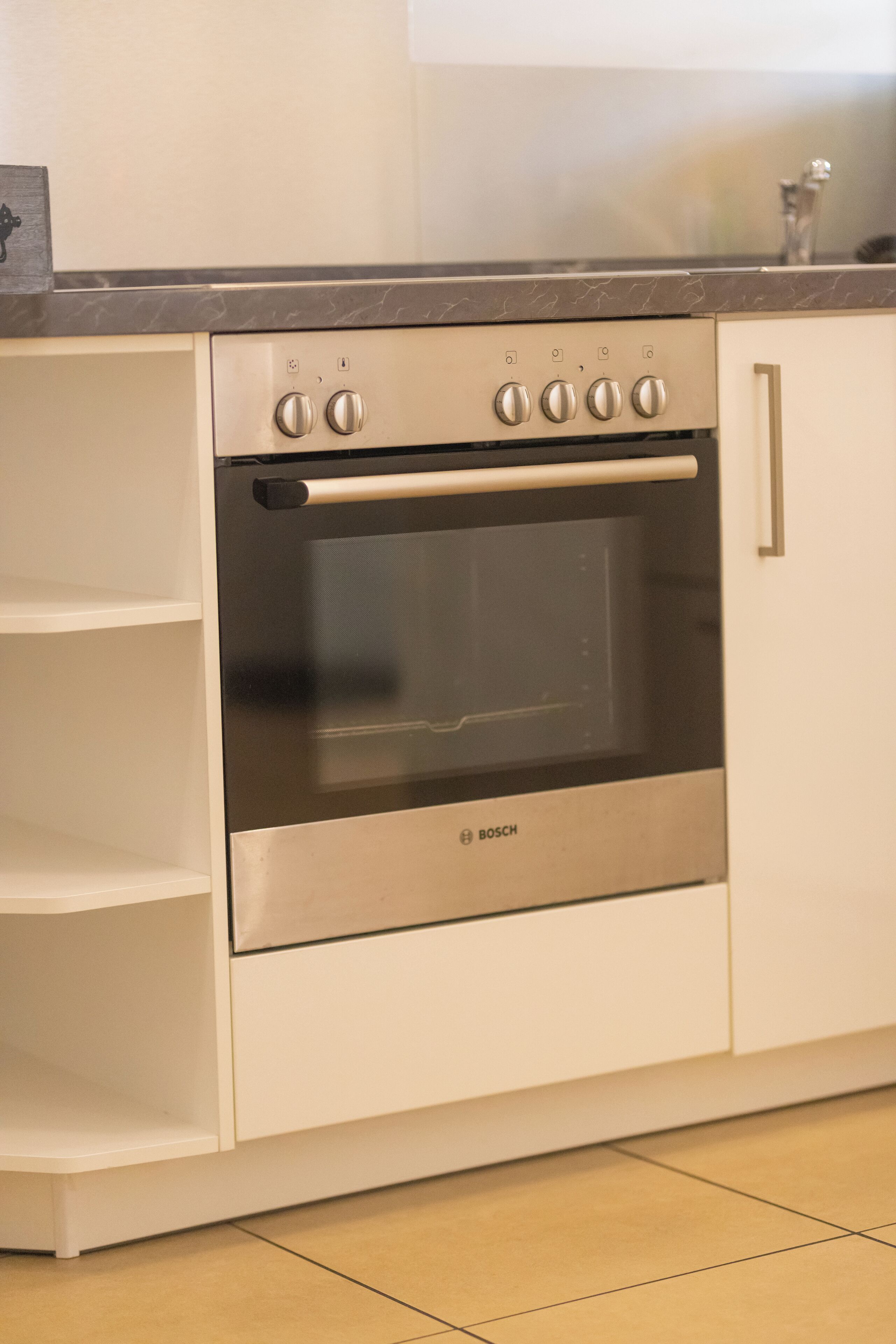 Uma cozinha compacta com forno Bosch, armários brancos e bancada de mármore.