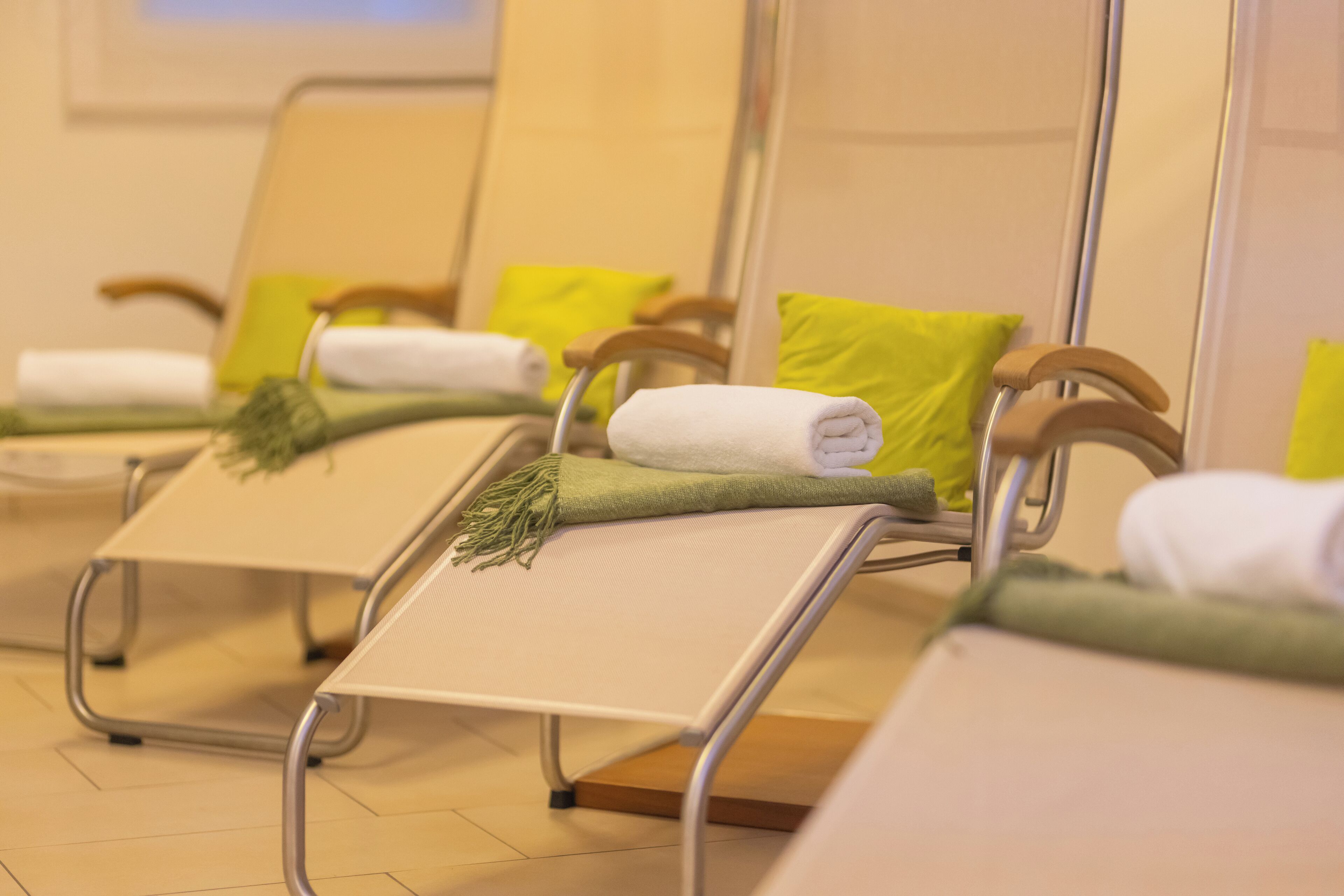 A row of reclining chairs with towels and green cushions, arranged in a waiting area.