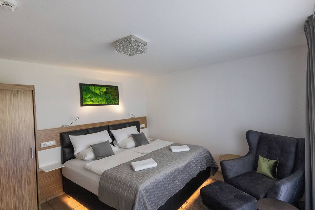 Ein modernes Schlafzimmer mit Bett, Sessel, Nachttisch und Kleiderschrank.