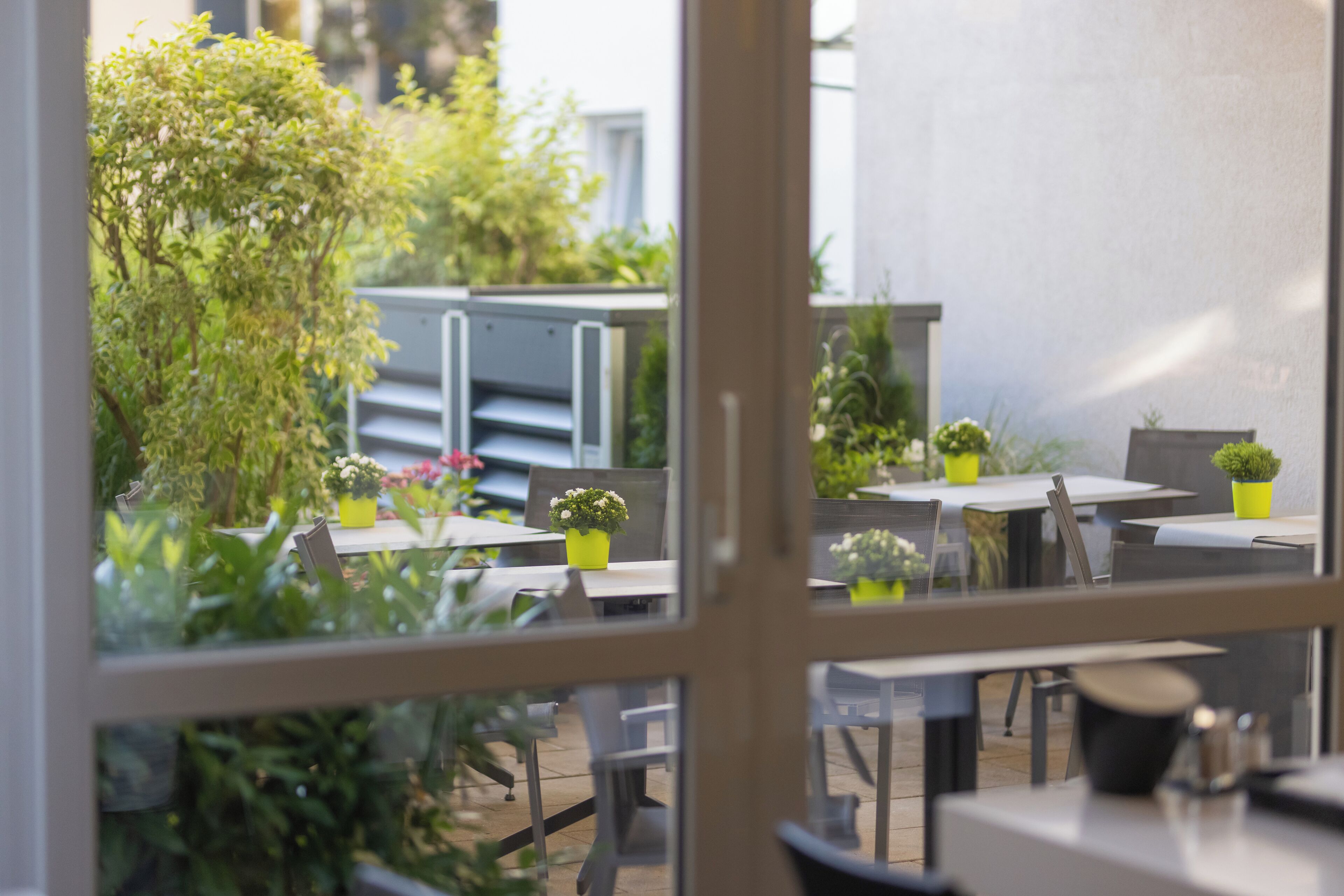 Un espace extérieur aménagé avec des tables et des chaises, entouré de plantes en pot et de verdure.