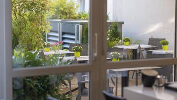 Un espace extérieur aménagé avec des tables et des chaises, entouré de plantes en pot et de verdure.