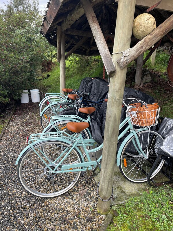A row of vintage bicycles parked under a wooden shelter with a rope and a basket attached to one.