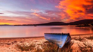 A boat on a sandy beach with a calm body of water and a sunset in the background. - Driftwood Cottages (Dover)