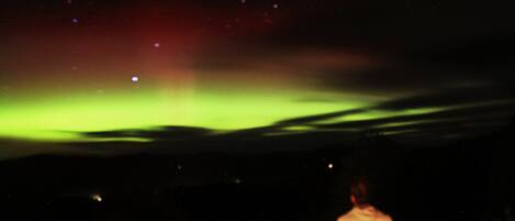 A person standing under a night sky with visible stars and a green aurora.