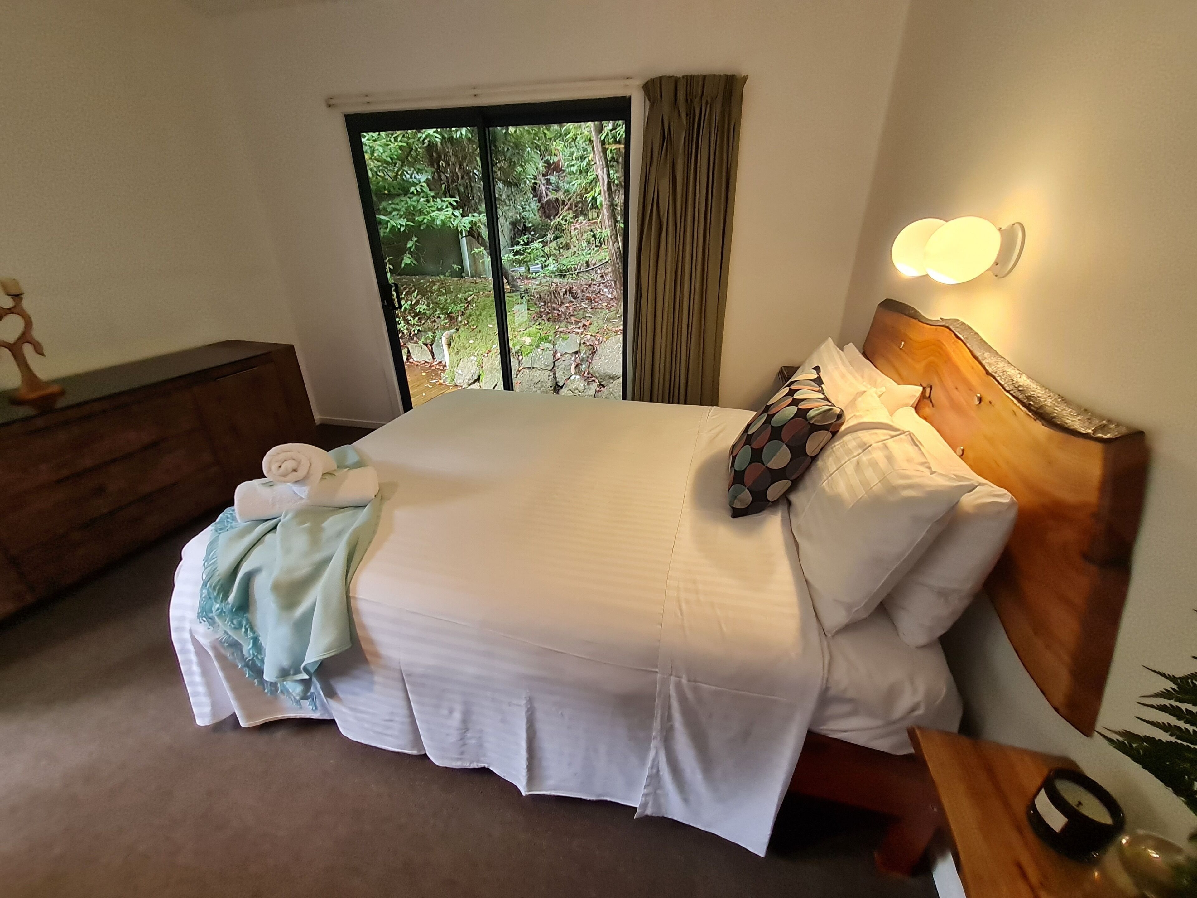 Een net opgemaakt bed met witte lakens, een houten hoofdbord en een nachtkastje met een lamp.