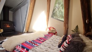 Una habitación acogedora con techo de madera, chimenea, cama con manta estampada y una ventana pequeña.
