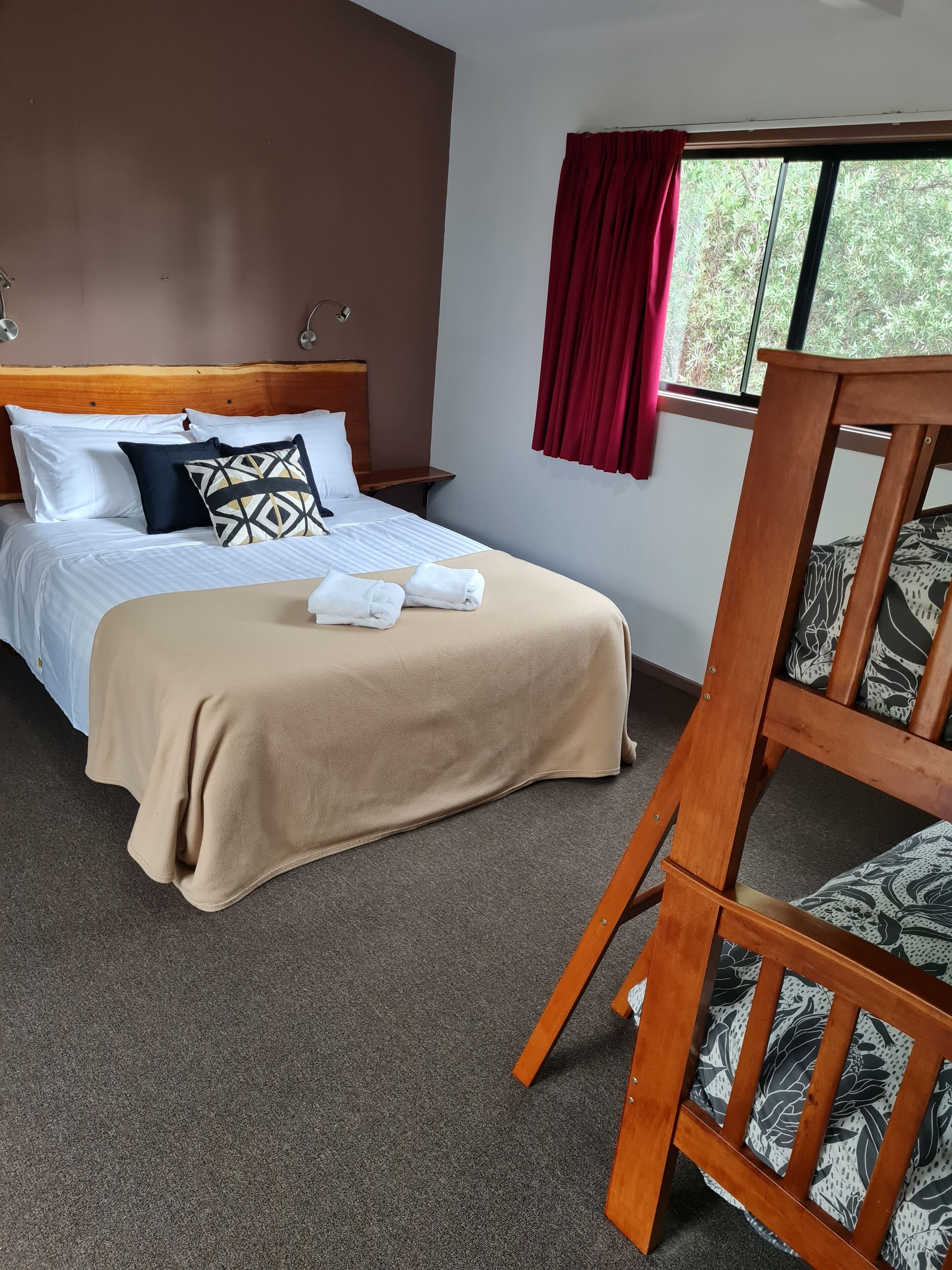 A neatly made bed with a beige blanket, white pillows, and a geometric-patterned pillow. There is a wooden chair with a floral cushion next to the bed.