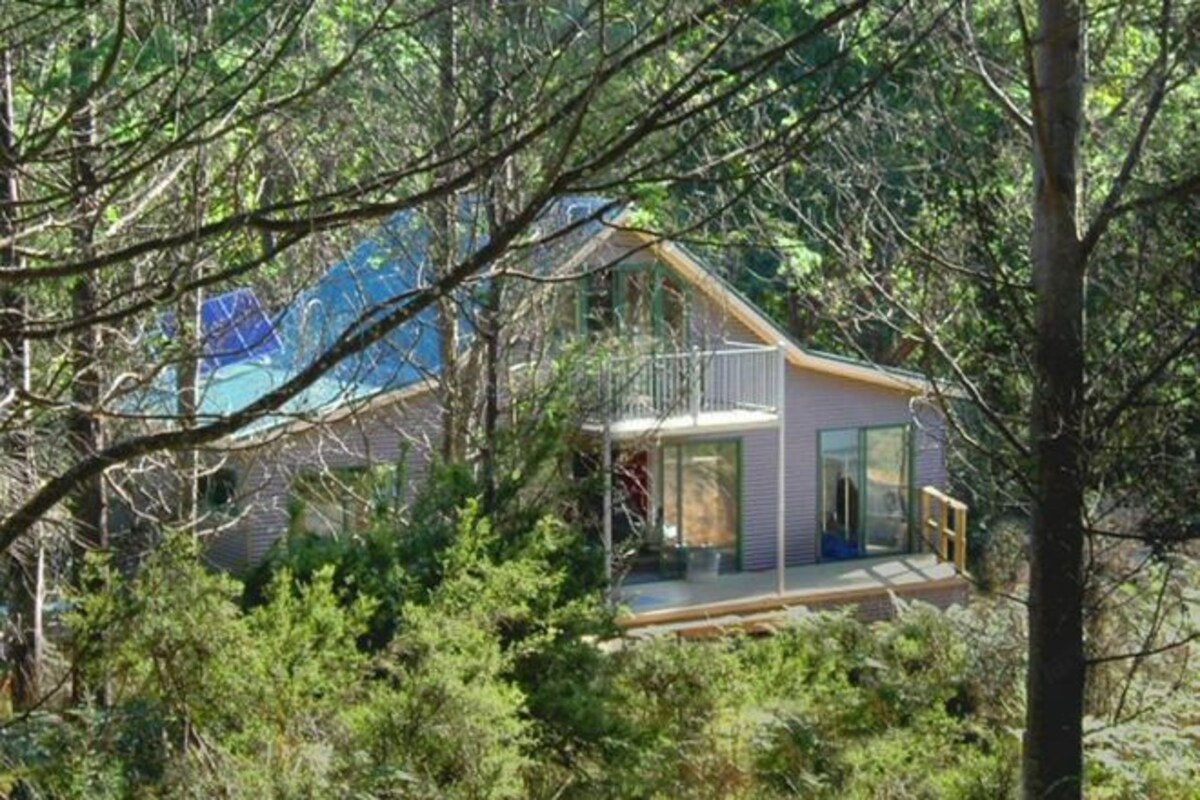 Una casa moderna con balcón de cristal, rodeada de abundante vegetación.