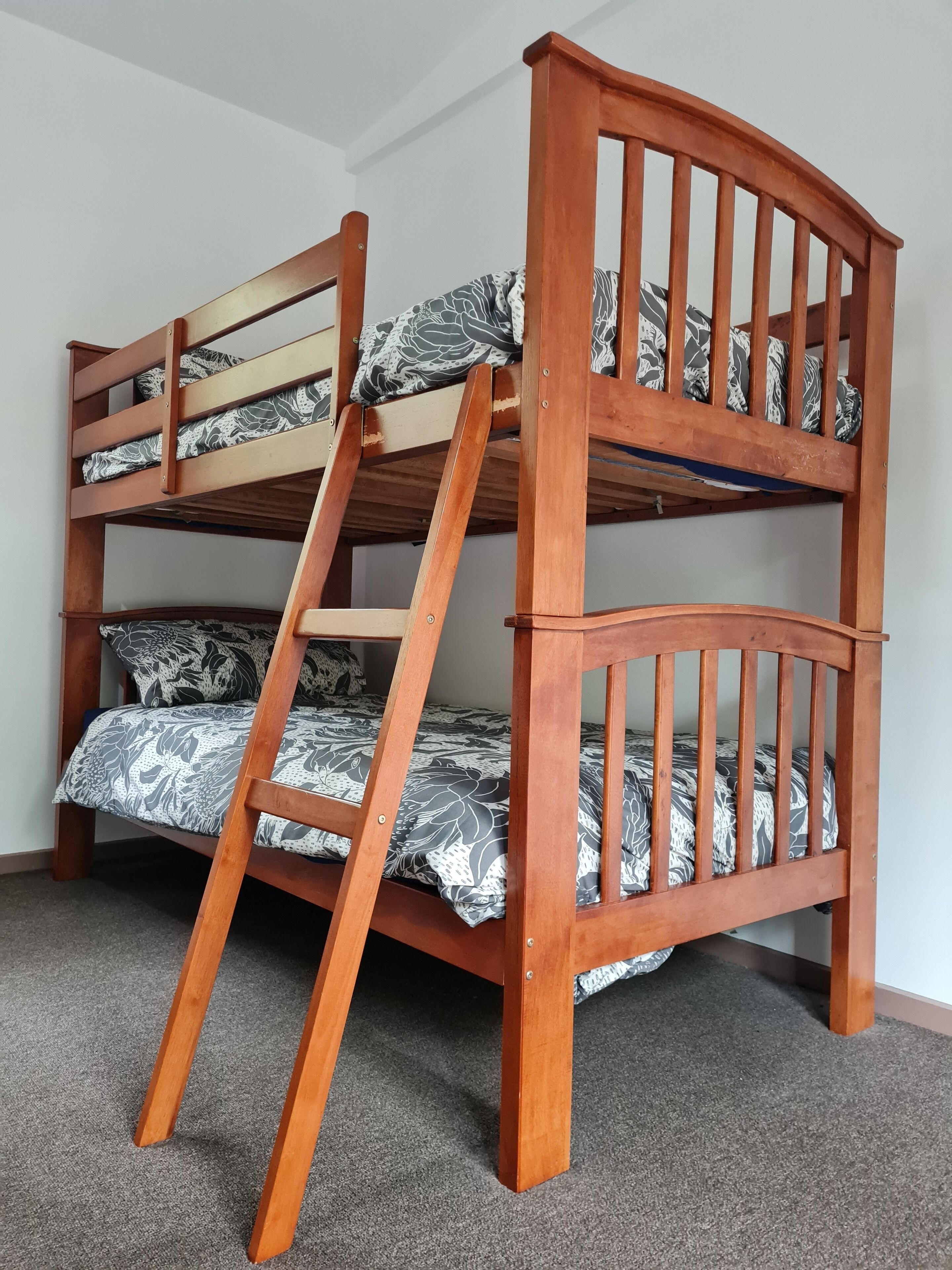 Un lit superposé avec une échelle, une structure en bois et une literie à motifs.