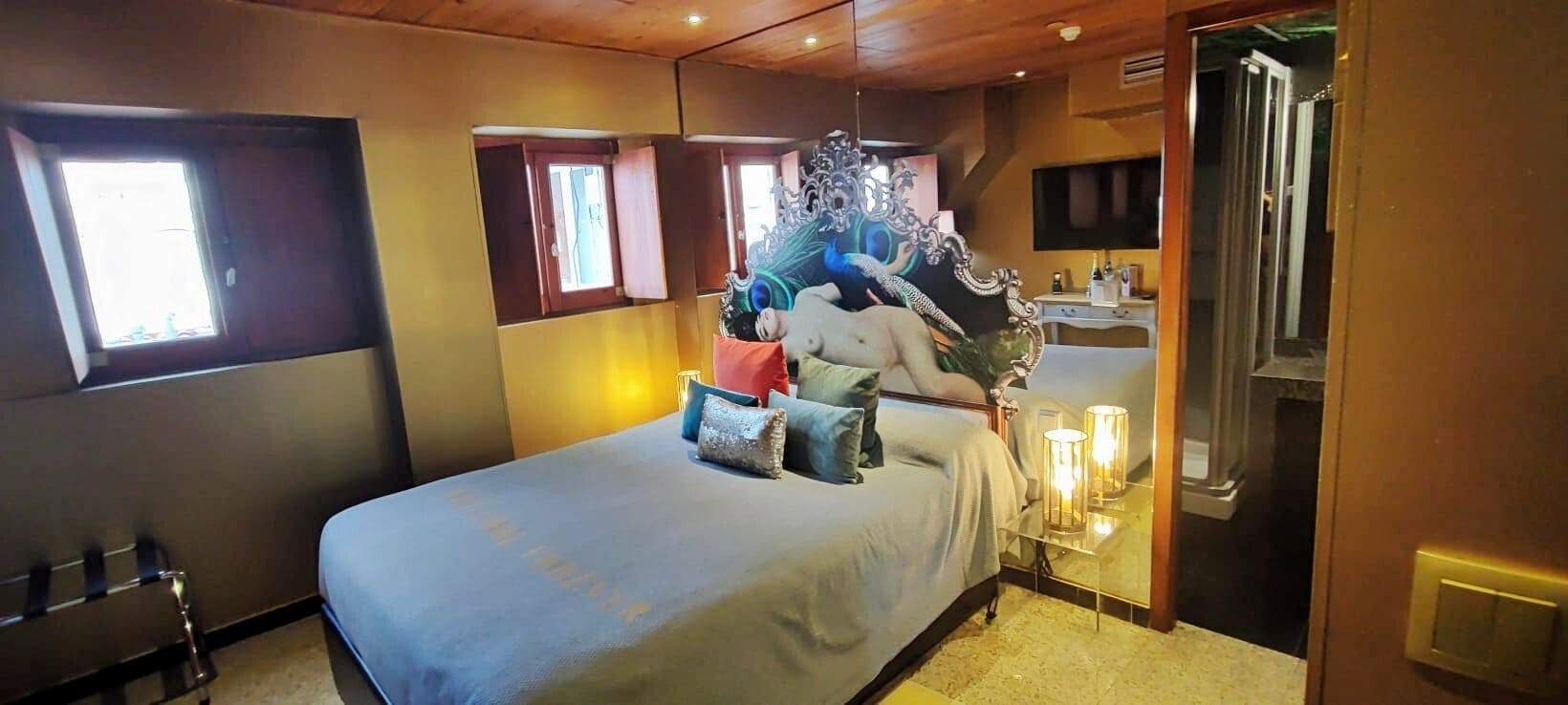 A bedroom with a bed, a mirror, a television, and a window.
