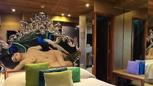 A bedroom with a large bed, a mirror, and a peacock headboard.