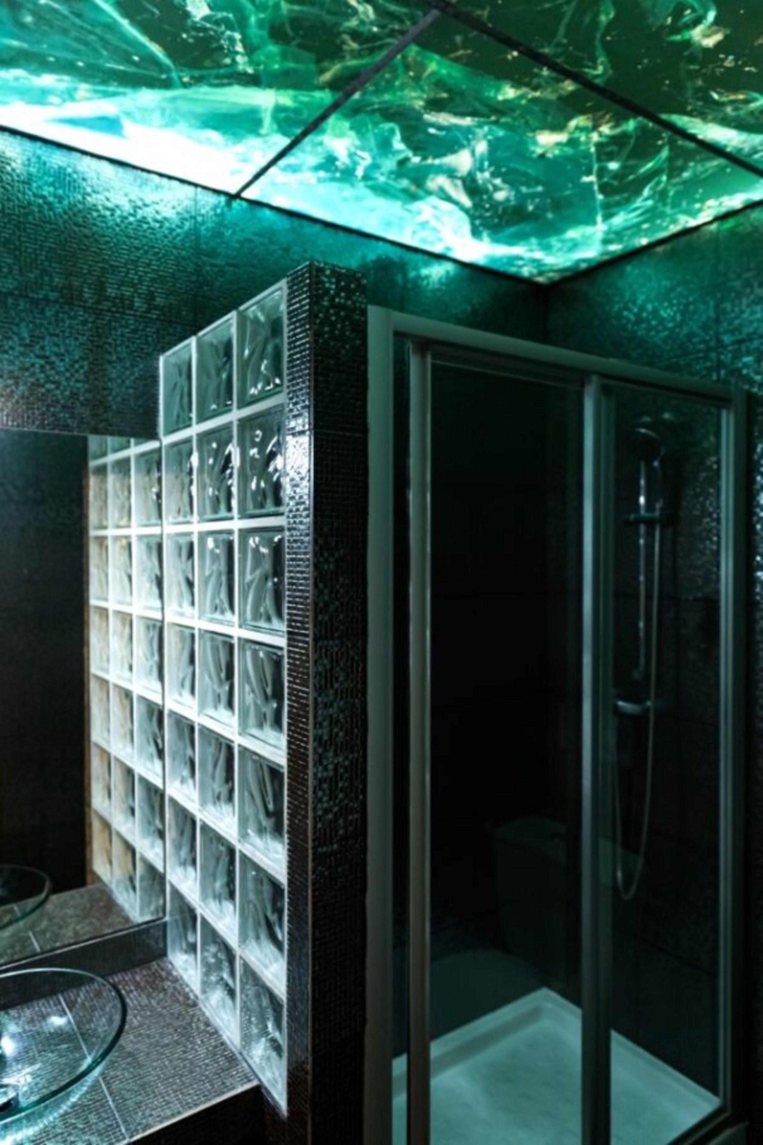 Une salle de bain dotée d’une douche à parois de verre, d’un mur recouvert de carreaux de verre et d’un lavabo en forme de bol également en verre.