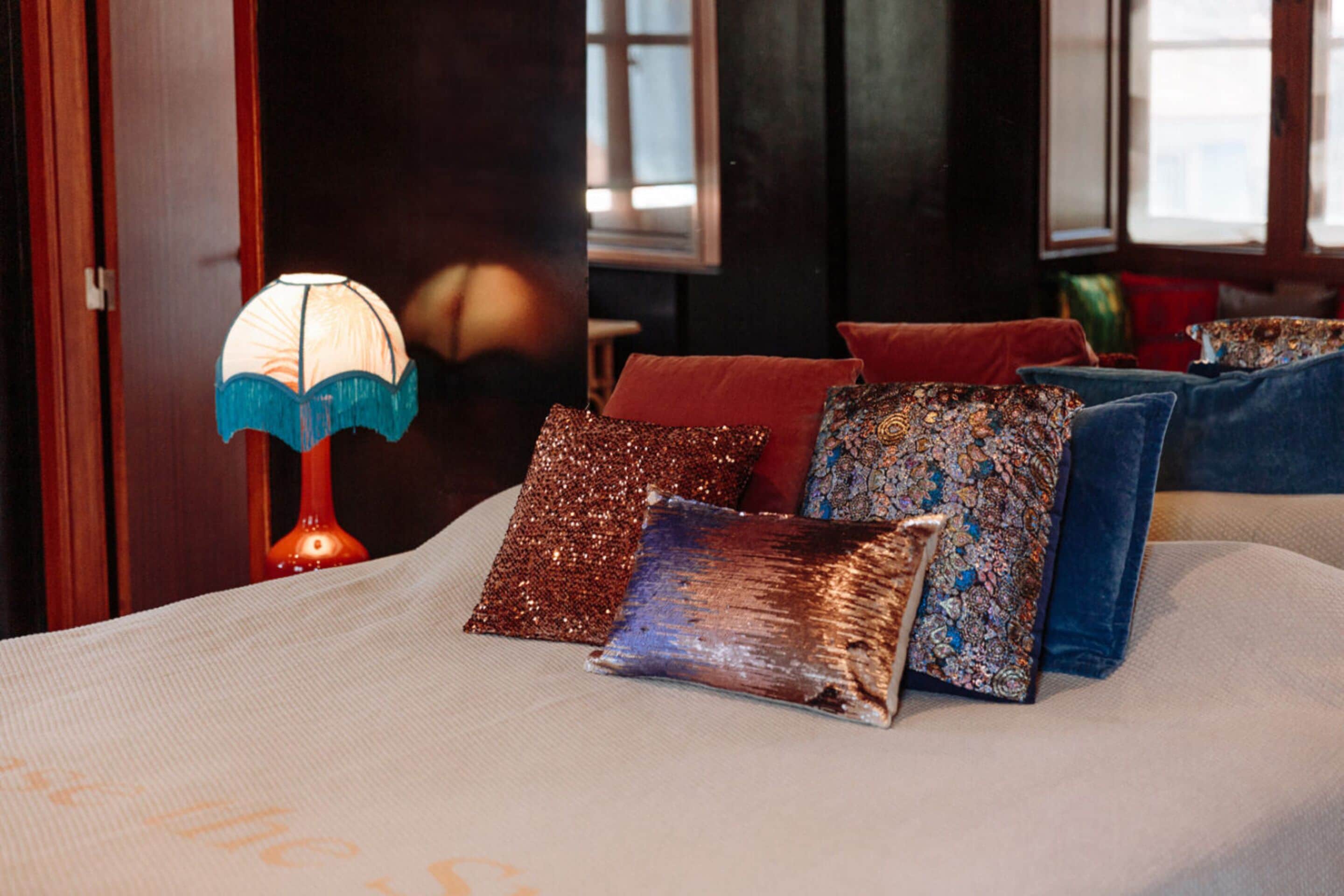 A bed with decorative pillows and a table lamp in a room with dark walls and windows.