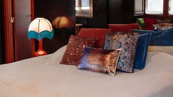 A bed with decorative pillows and a table lamp in a room with dark walls and windows.