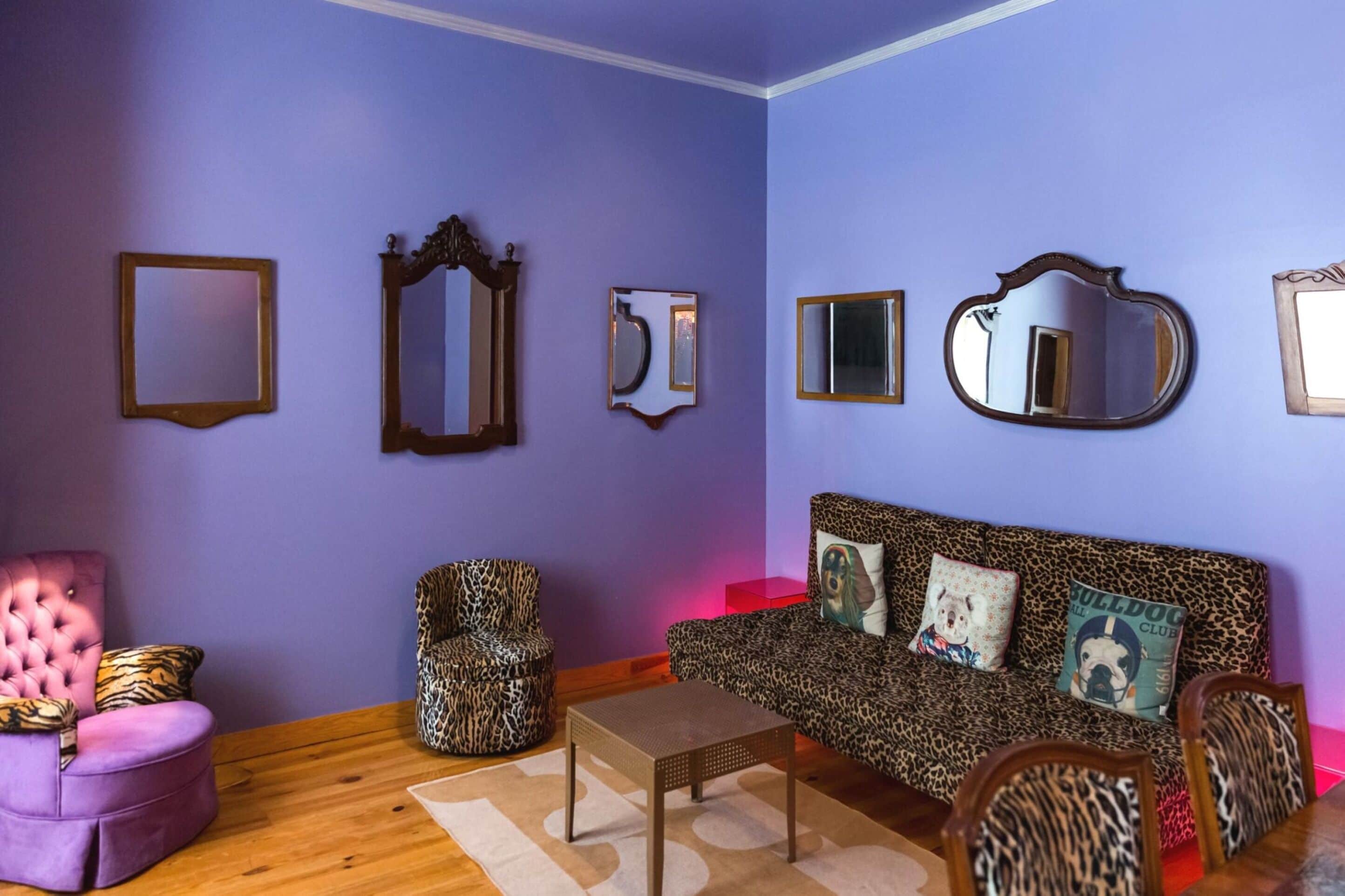 A room with a purple wall, a leopard print sofa, a pink chair, and a wooden coffee table.
