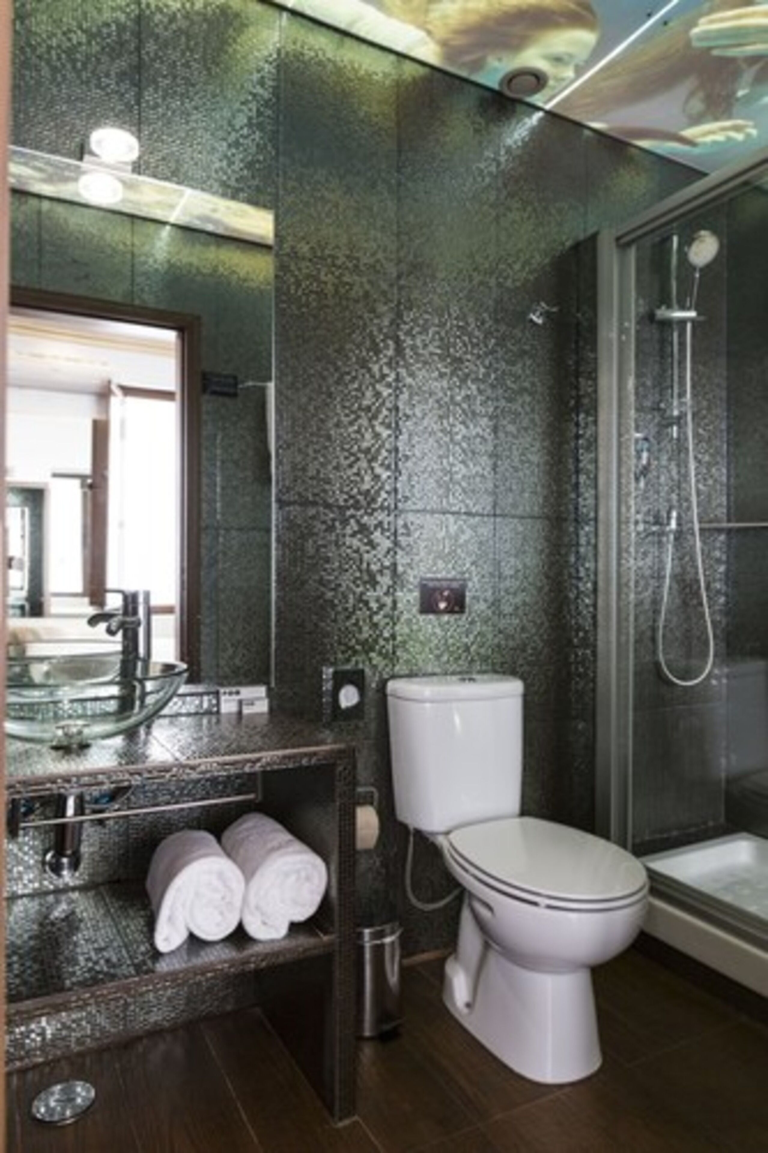 A modern bathroom with a glass sink, white toilet, and a shower area.
