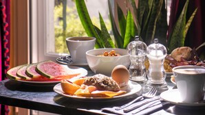 A breakfast table with various food items and a cup of coffee, positioned near a window with a view of buildings and trees.