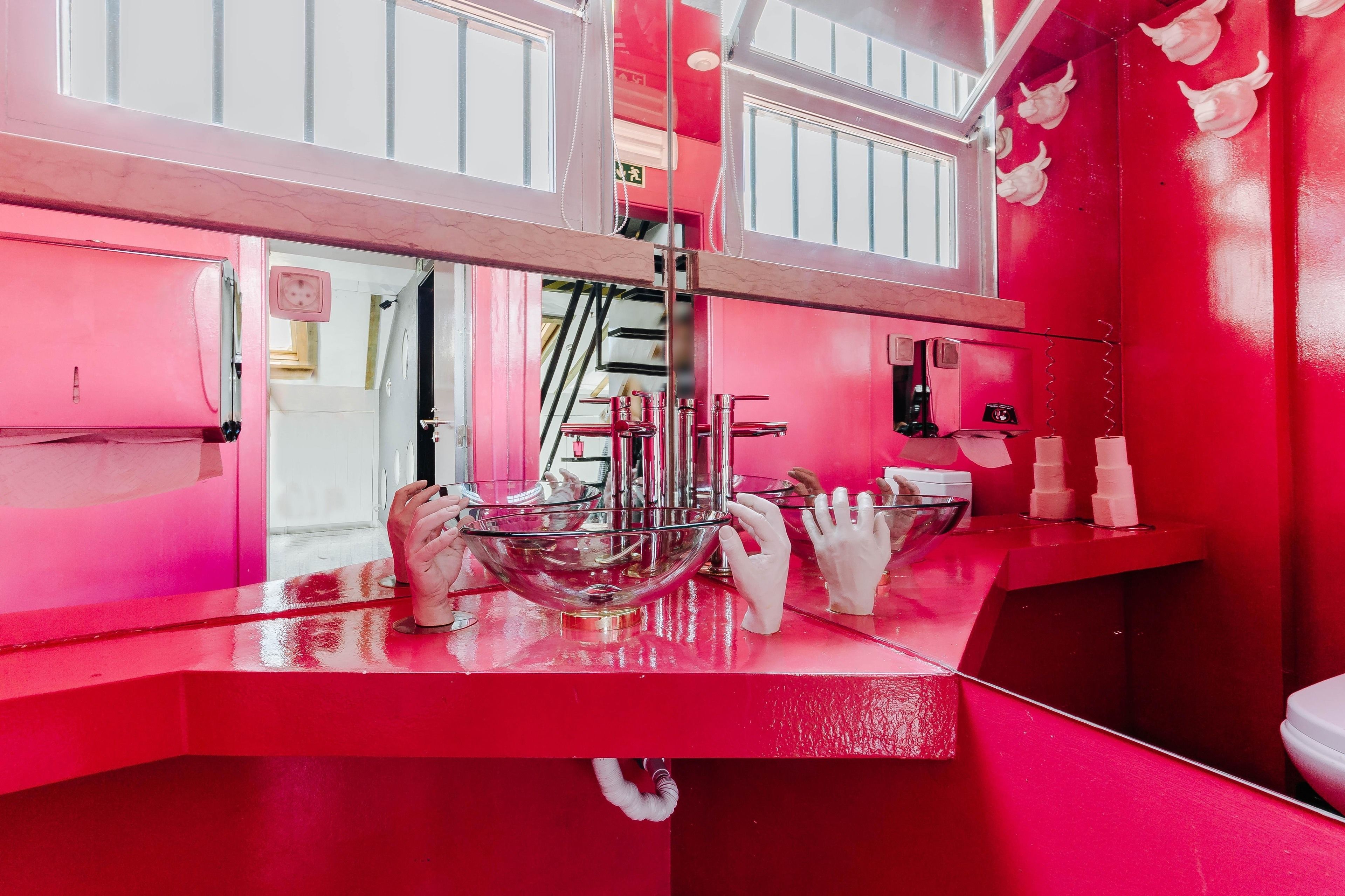 A bathroom with a red color scheme, a glass bowl sink, and a hand dryer.