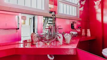 A bathroom with a red color scheme, a glass bowl sink, and a hand dryer.
