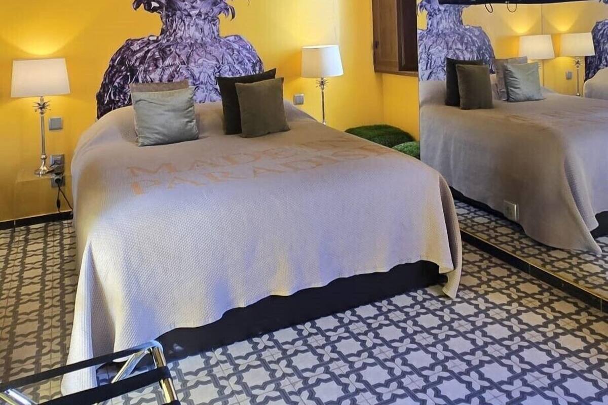 Habitación de hotel con una cama grande, un espejo, una planta en maceta y un piso con diseño.