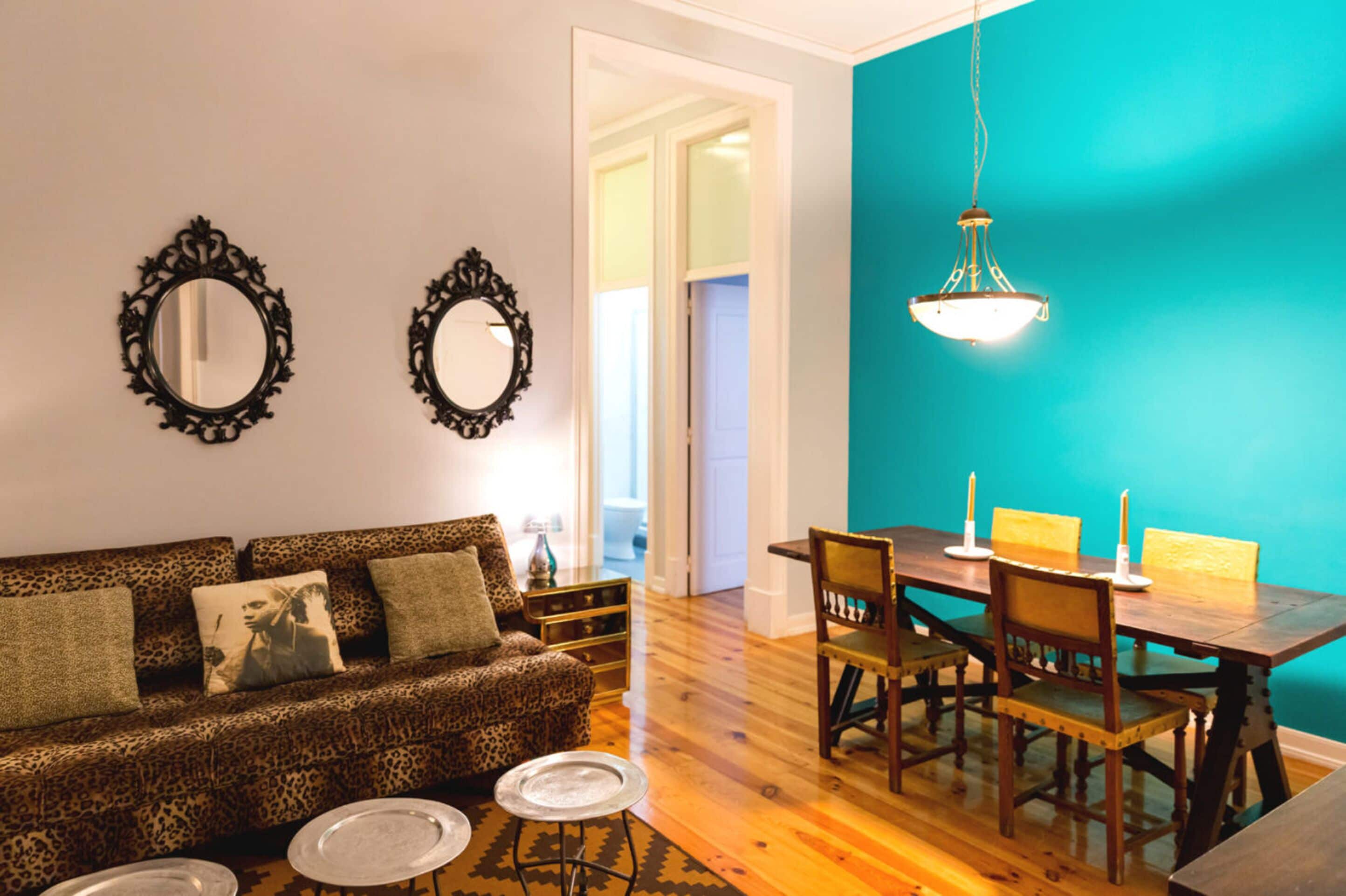 Un salon comprenant un canapé, une table à manger avec des chaises et deux miroirs fixés au mur.