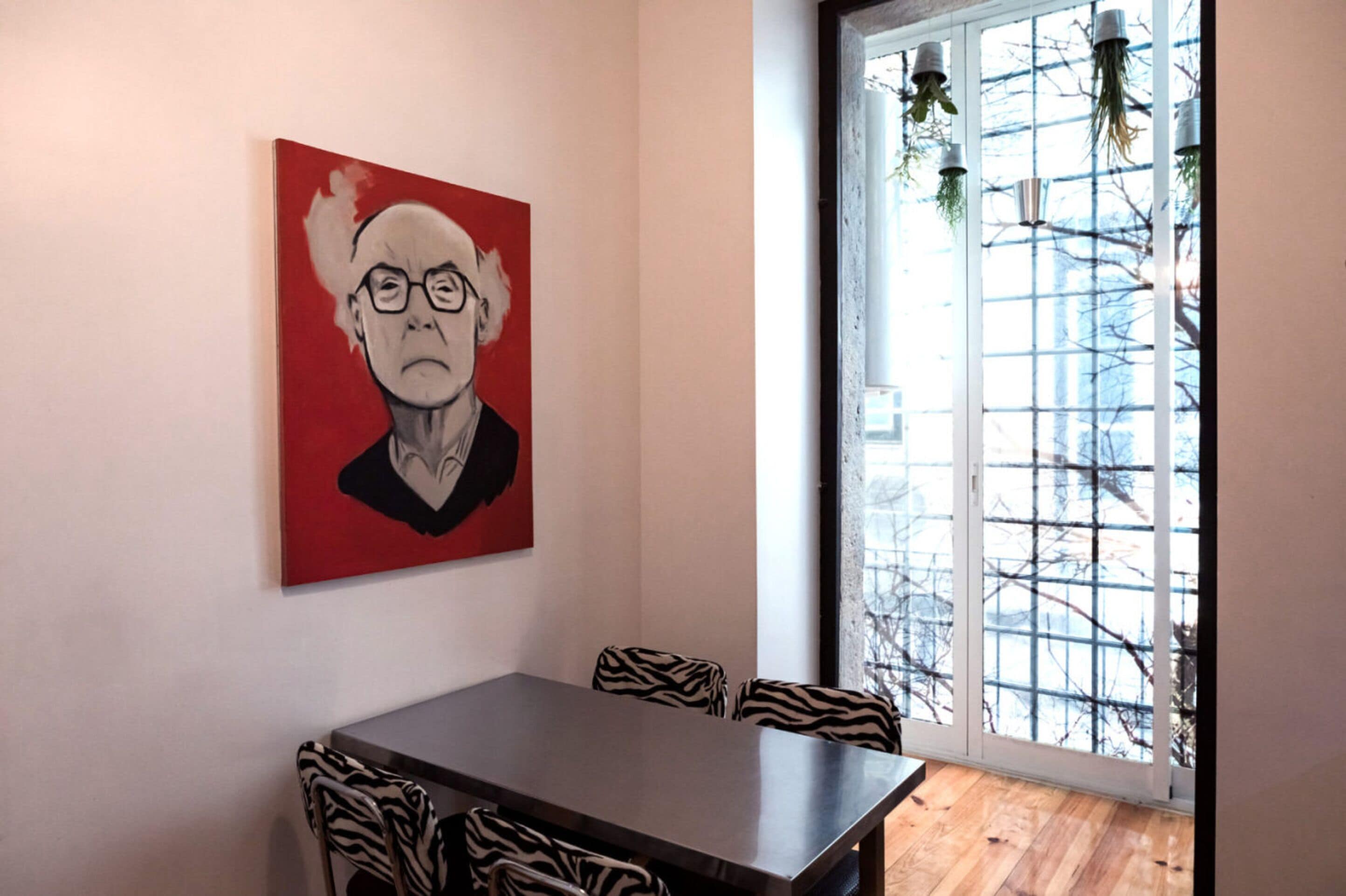 A dining area with a zebra-striped table and chairs, a red painting on the wall, and a view through a glass door.