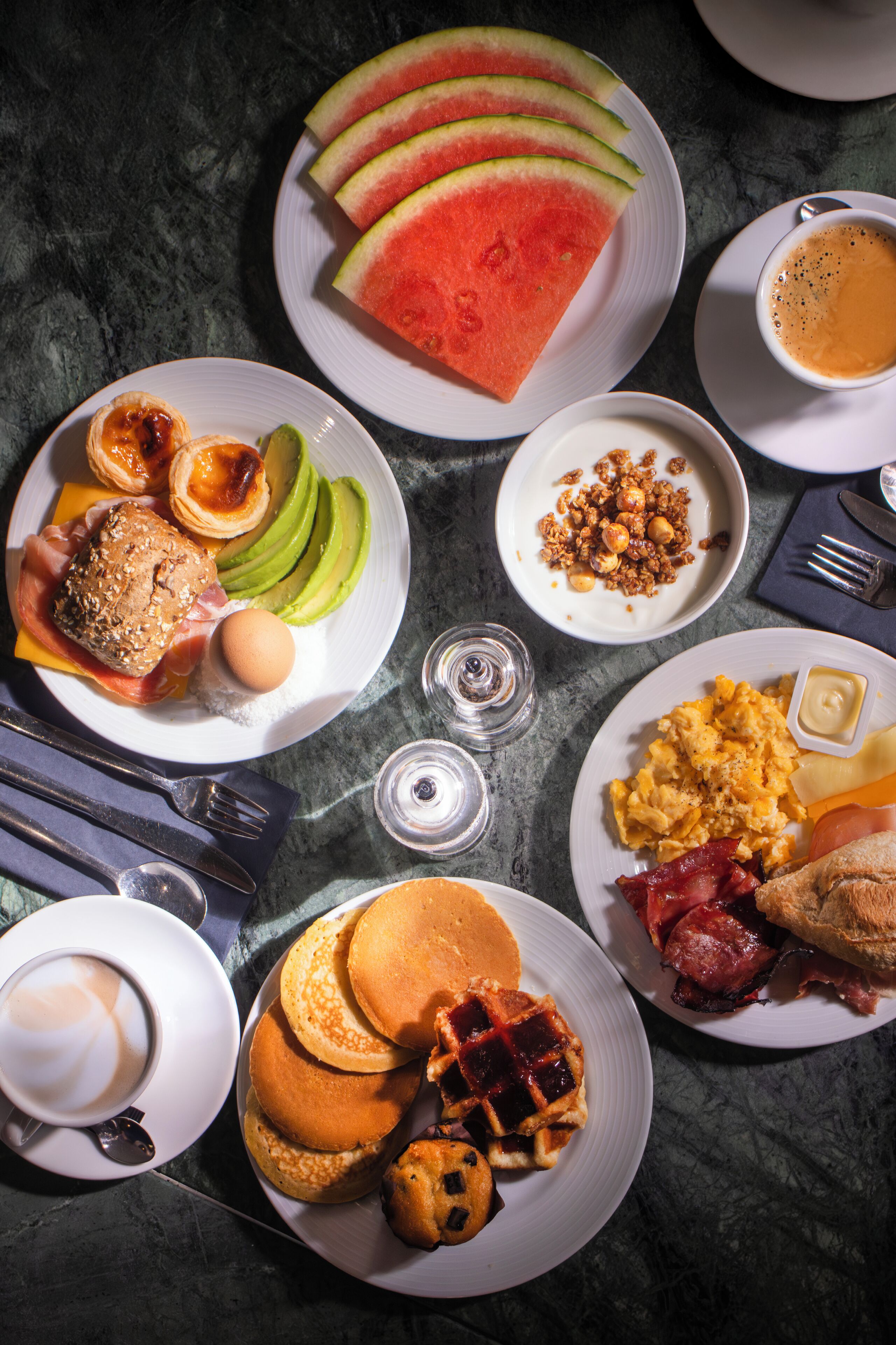Una mesa de desayuno con diversos platos, incluyendo panqueques, huevos, tocino y tostadas.