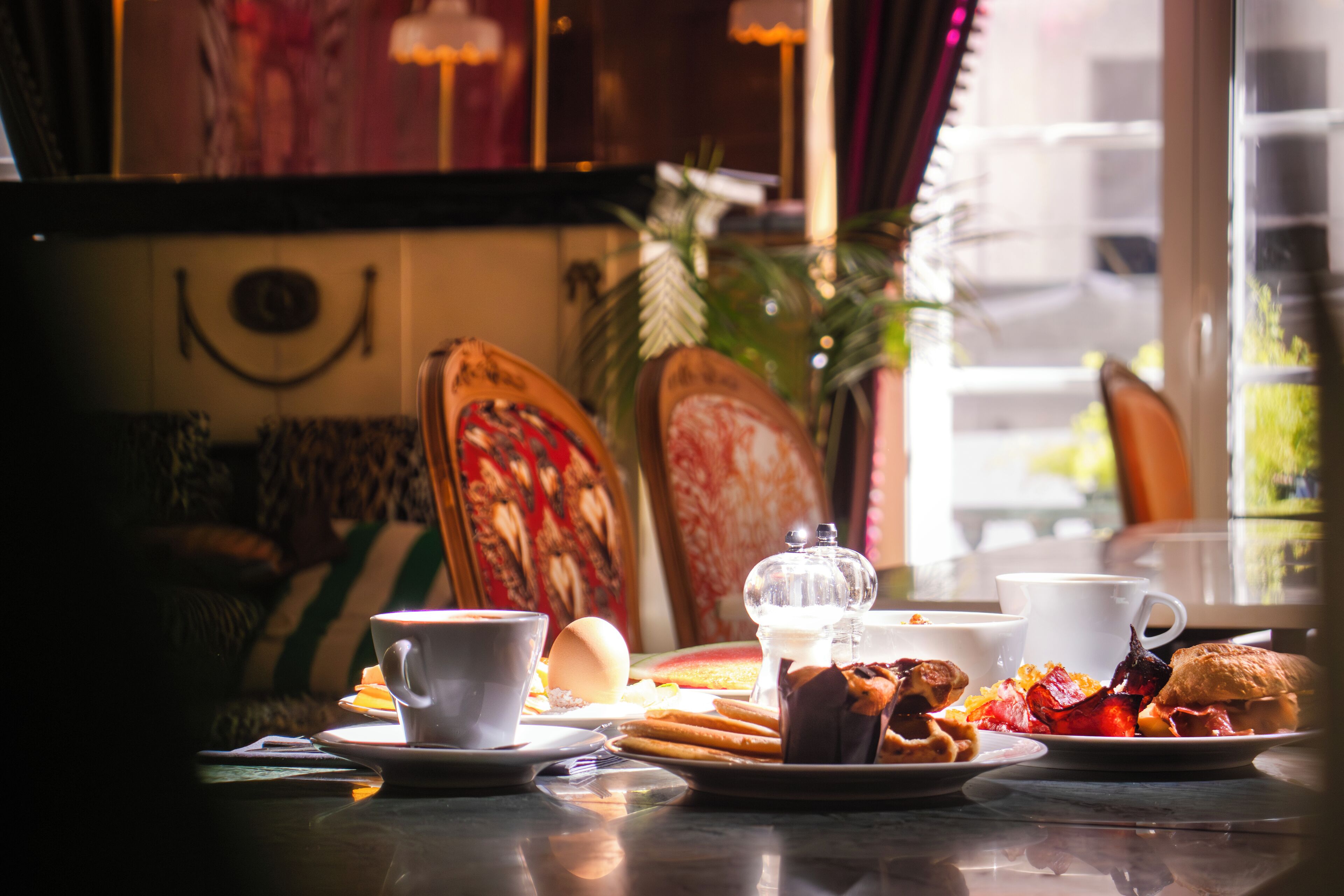 A breakfast setting with a coffee cup, croissant, and a plate of eggs and bacon.