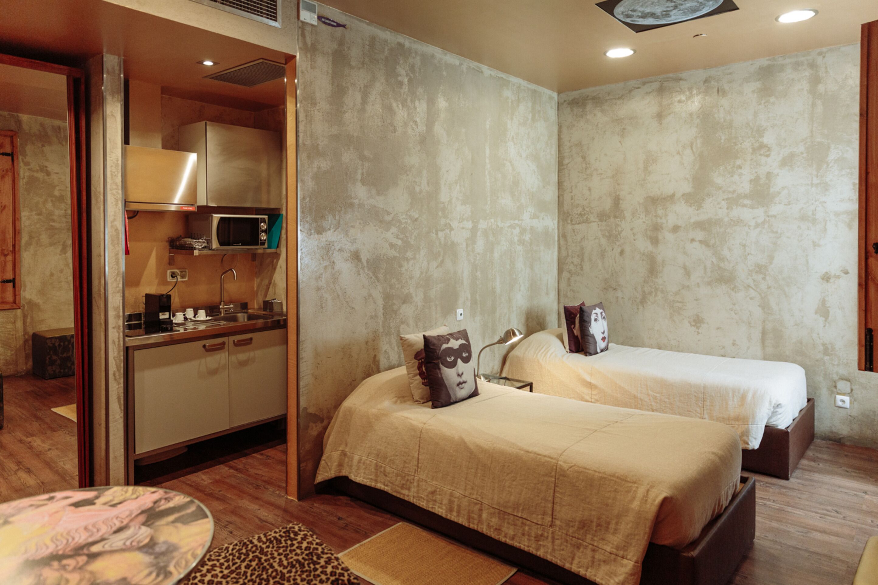 A compact hotel room with a kitchenette, two beds, and a small round table.