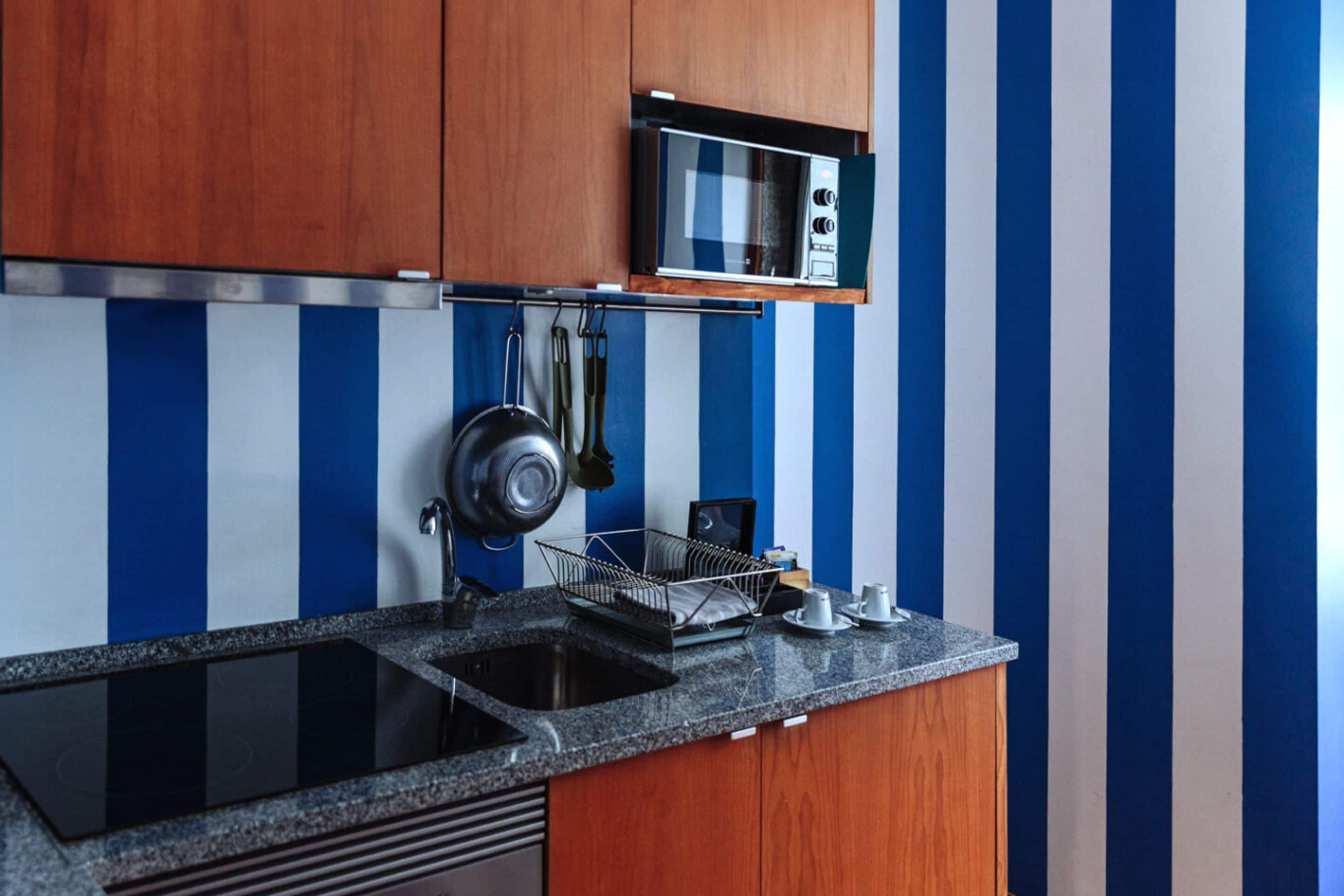 Una cocina con armarios de madera, un lavamanos negro, un microondas y un salpicadero a rayas.