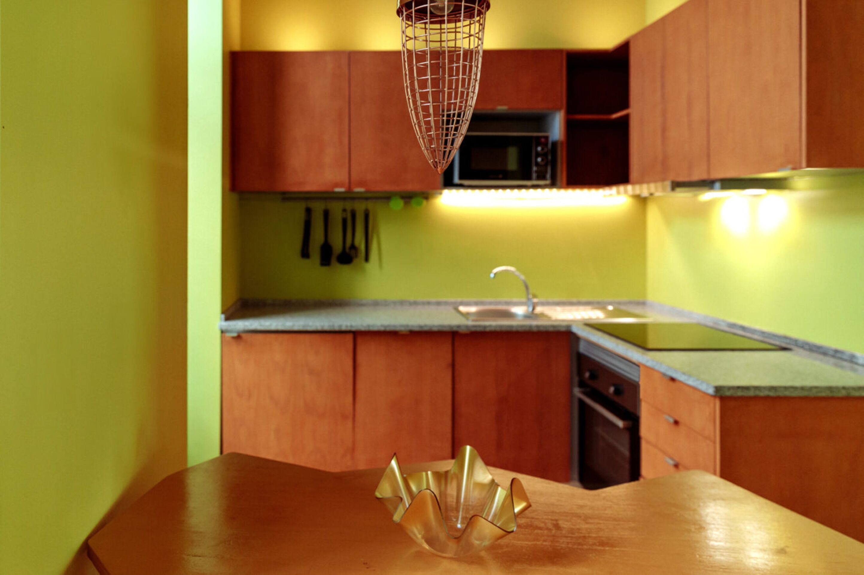 A kitchen with wooden cabinets, a microwave, a sink, and a decorative glass bowl on the counter.