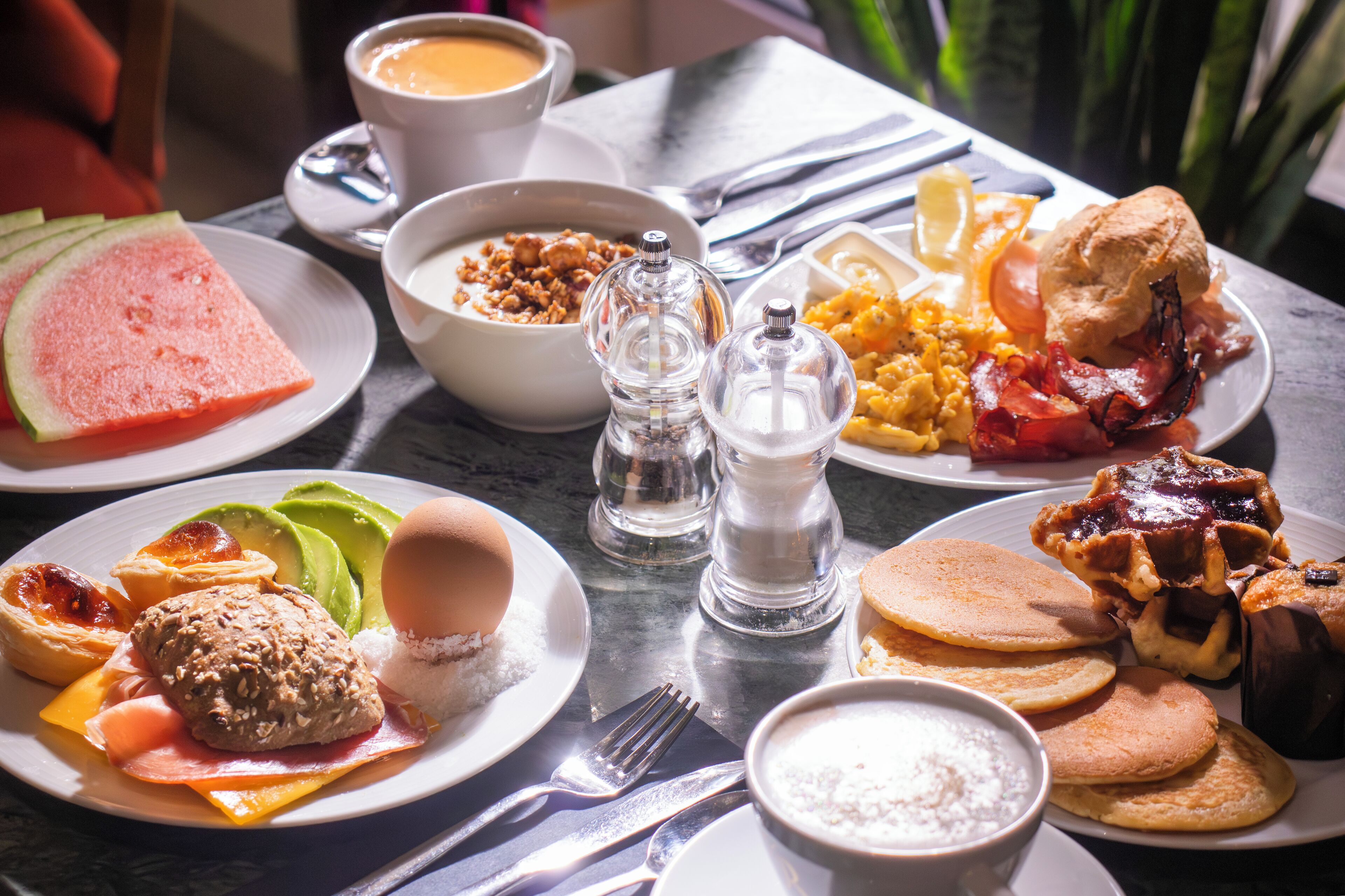 A breakfast table with various dishes including pancakes, eggs, bacon, and toast.