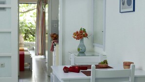 A white dining area with a table, chairs, a vase with flowers, and a mirror on the wall. - Ninetta's Studios (Poros)