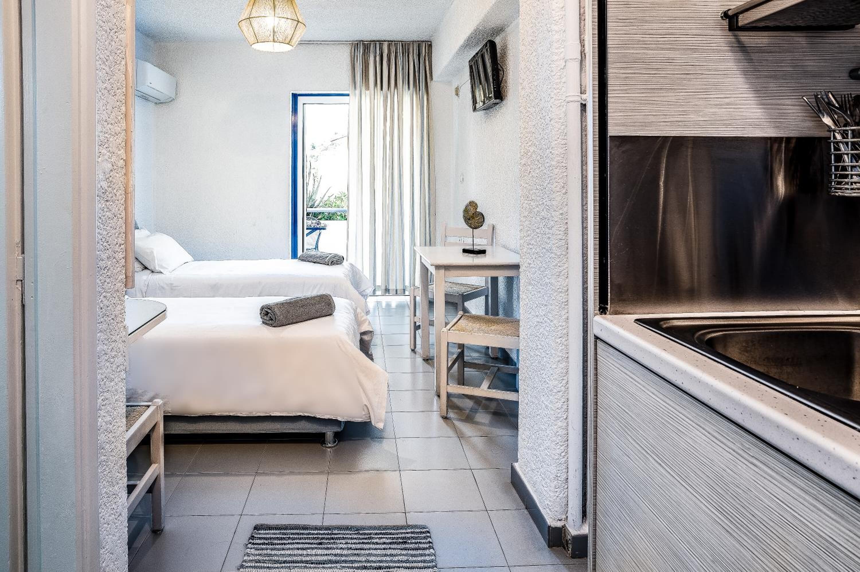 A compact hotel room with a bed, a small table, a chair, and a kitchenette.