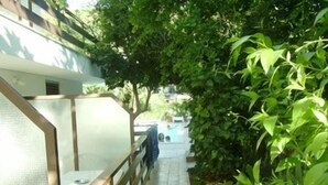 A narrow pathway flanked by lush green foliage and a white building with a metal railing. - Ninetta's Studios (Poros)